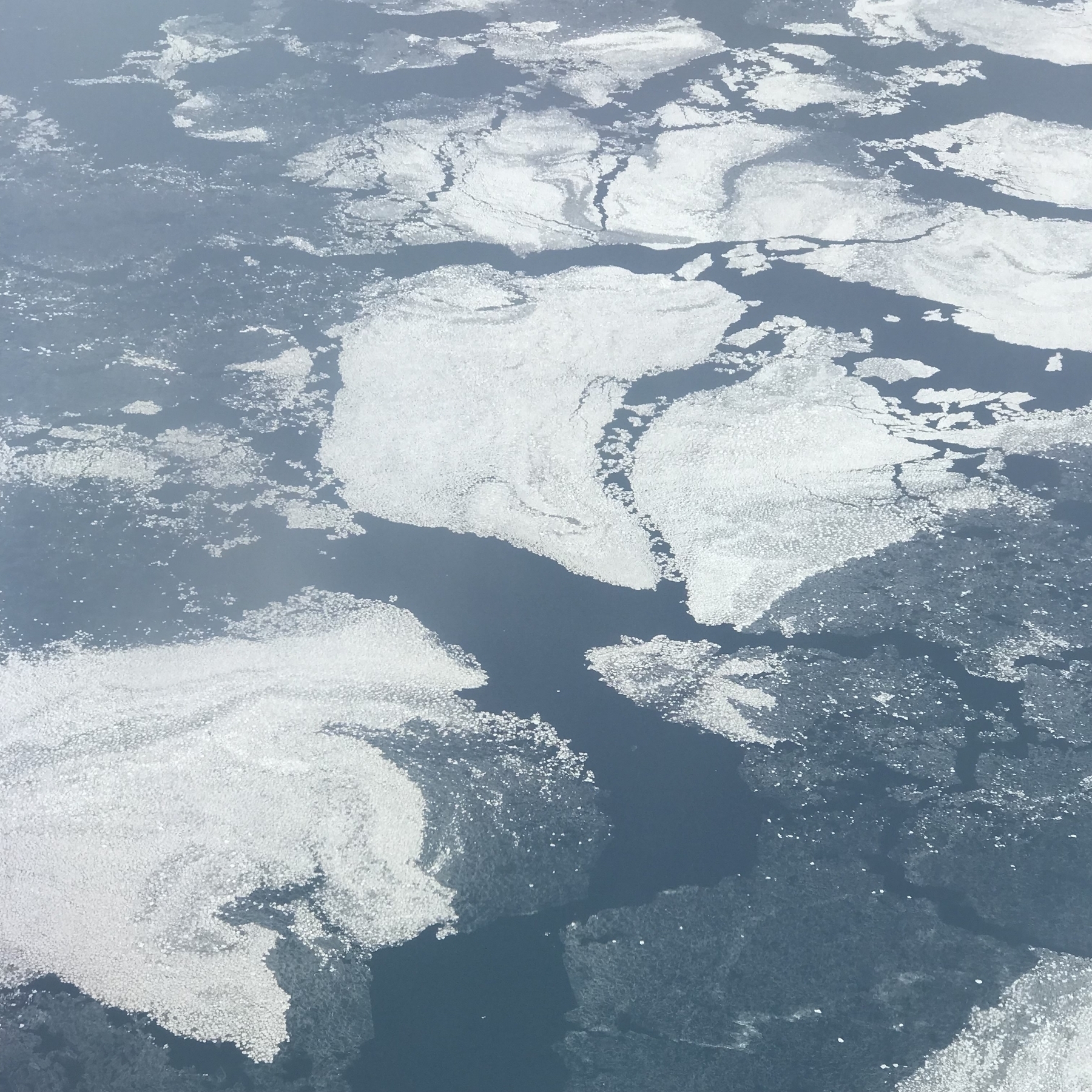 An aerial photo of Lake Michigan in the winter. Ice sheets of various sizes and densities cover most of the lake's surface.