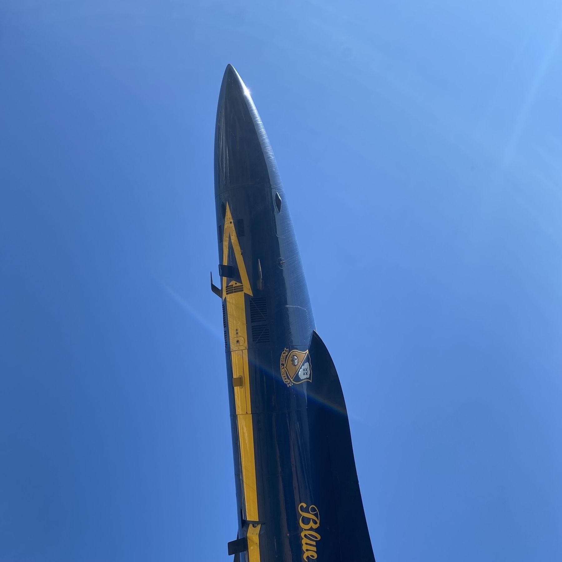 The front portion of an F18 fighter jet in Blue Angels livery against a blue sky.