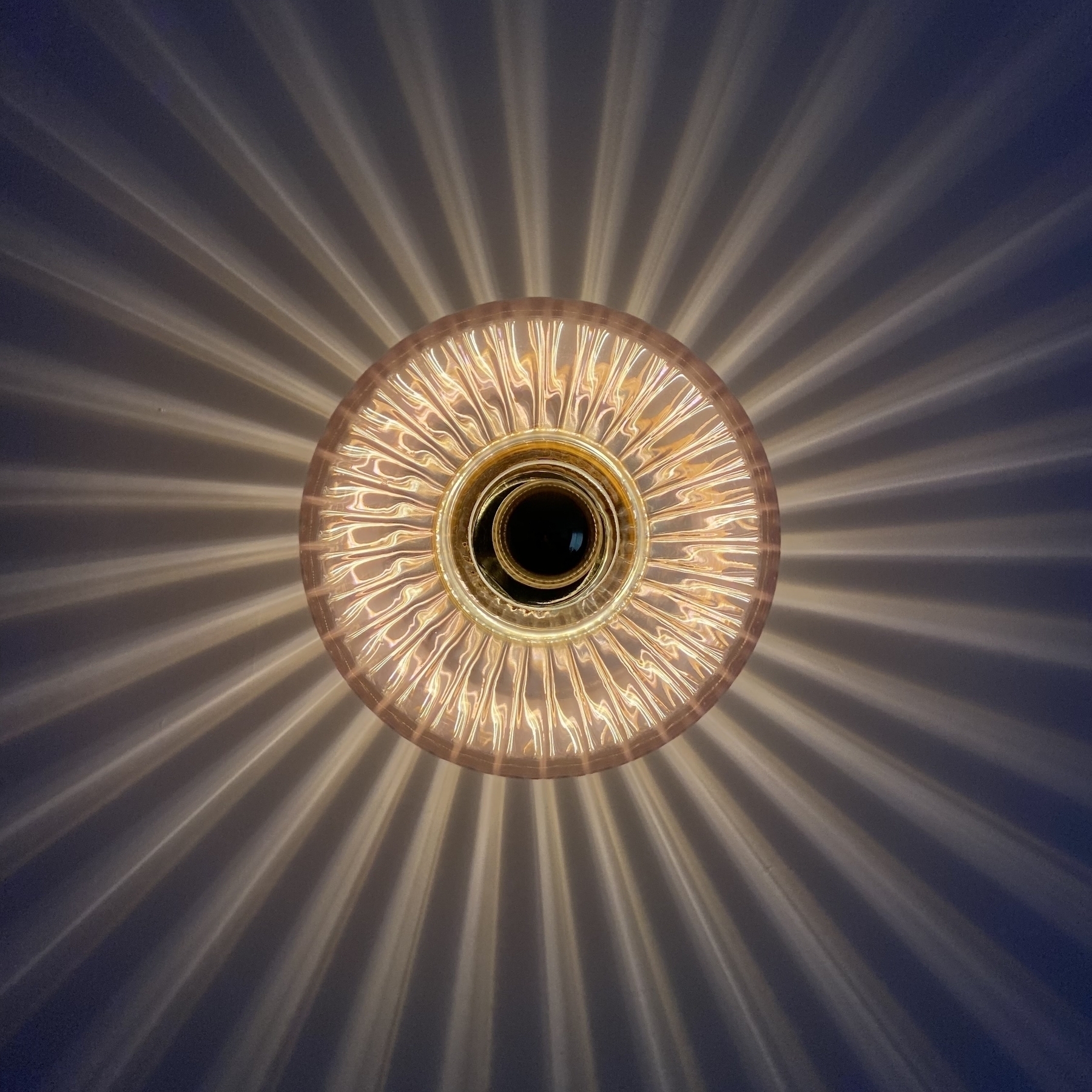A wall mounted circular glass light fixture with 33 equidistant rays shooting out from around the circle in all directions. 