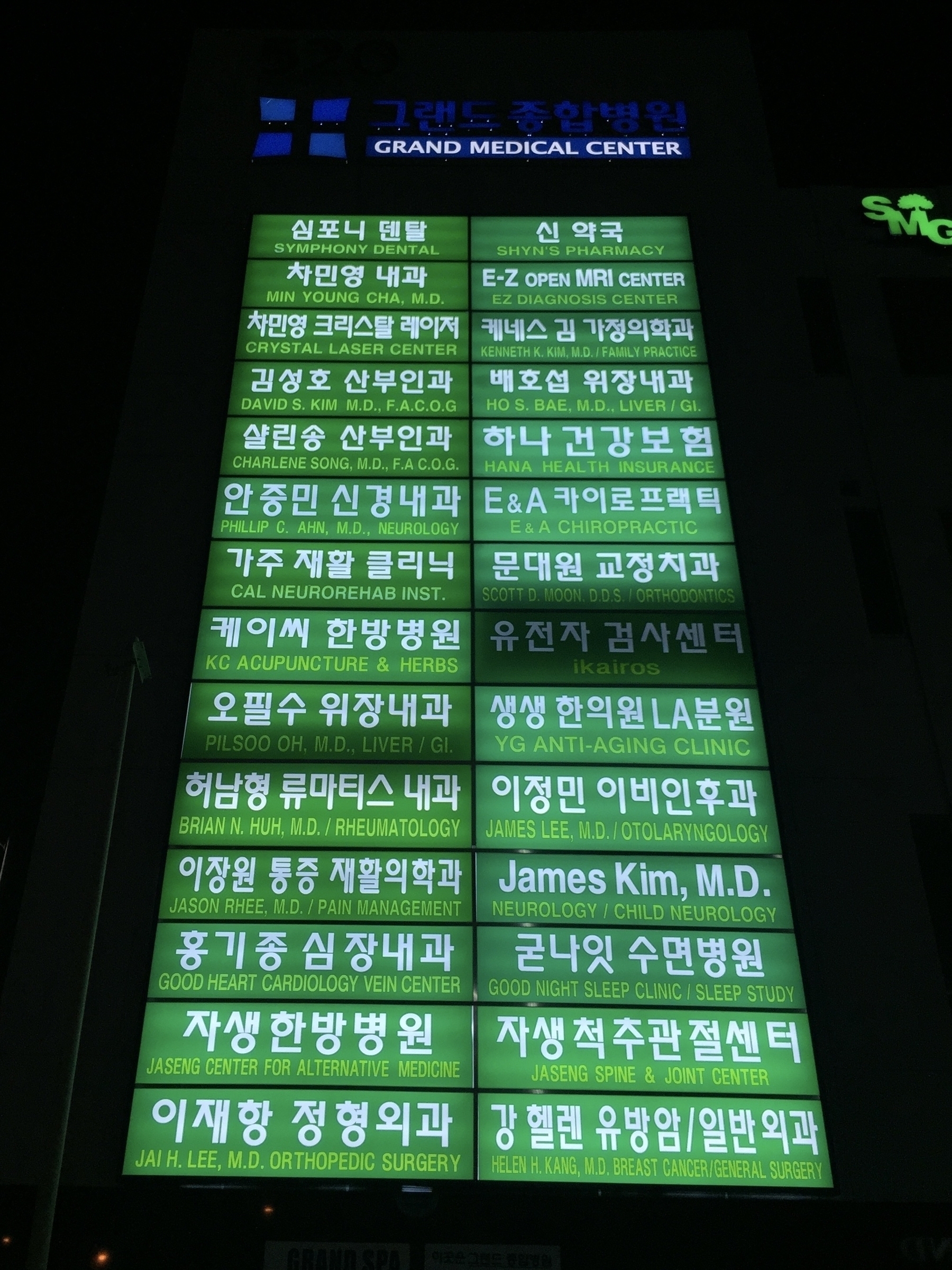 A tall outdoor sign for a medical center with a green glowing background. The sign lists 28 different offices in Korean and English in white lettering, including Jaseng Spine Center.