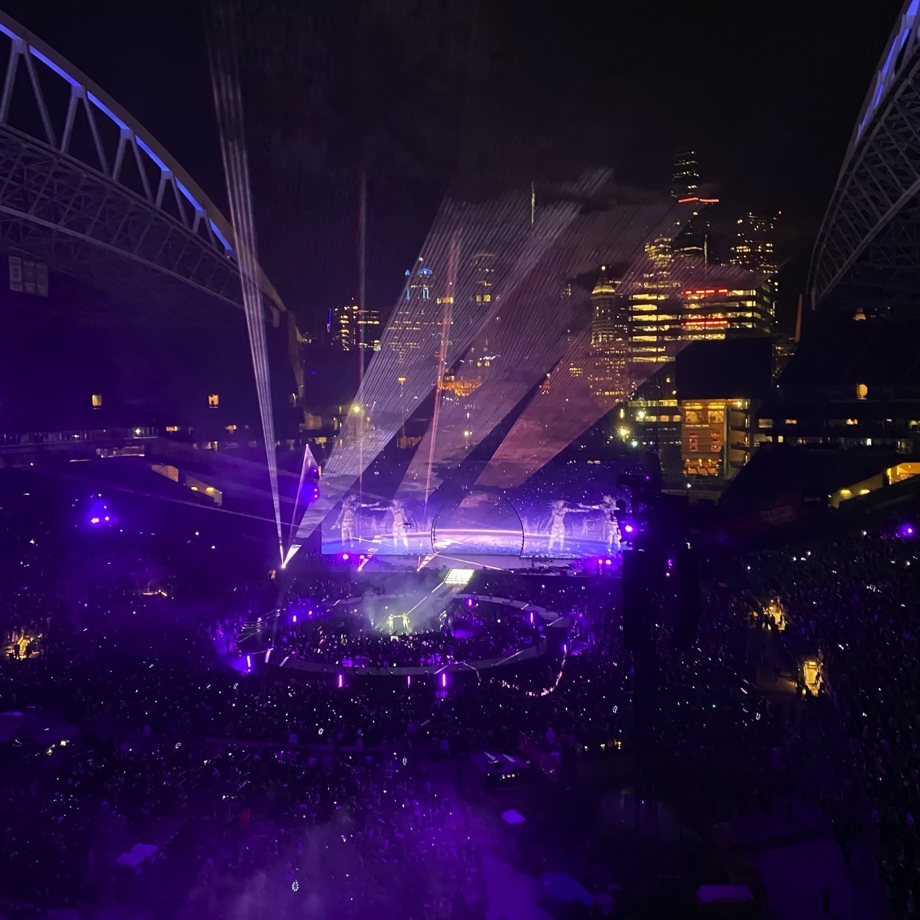 A wide shot of Lumen Field during Beyonce. Warm purple ambience with skinny white lights shining up into the Seattle skyline.