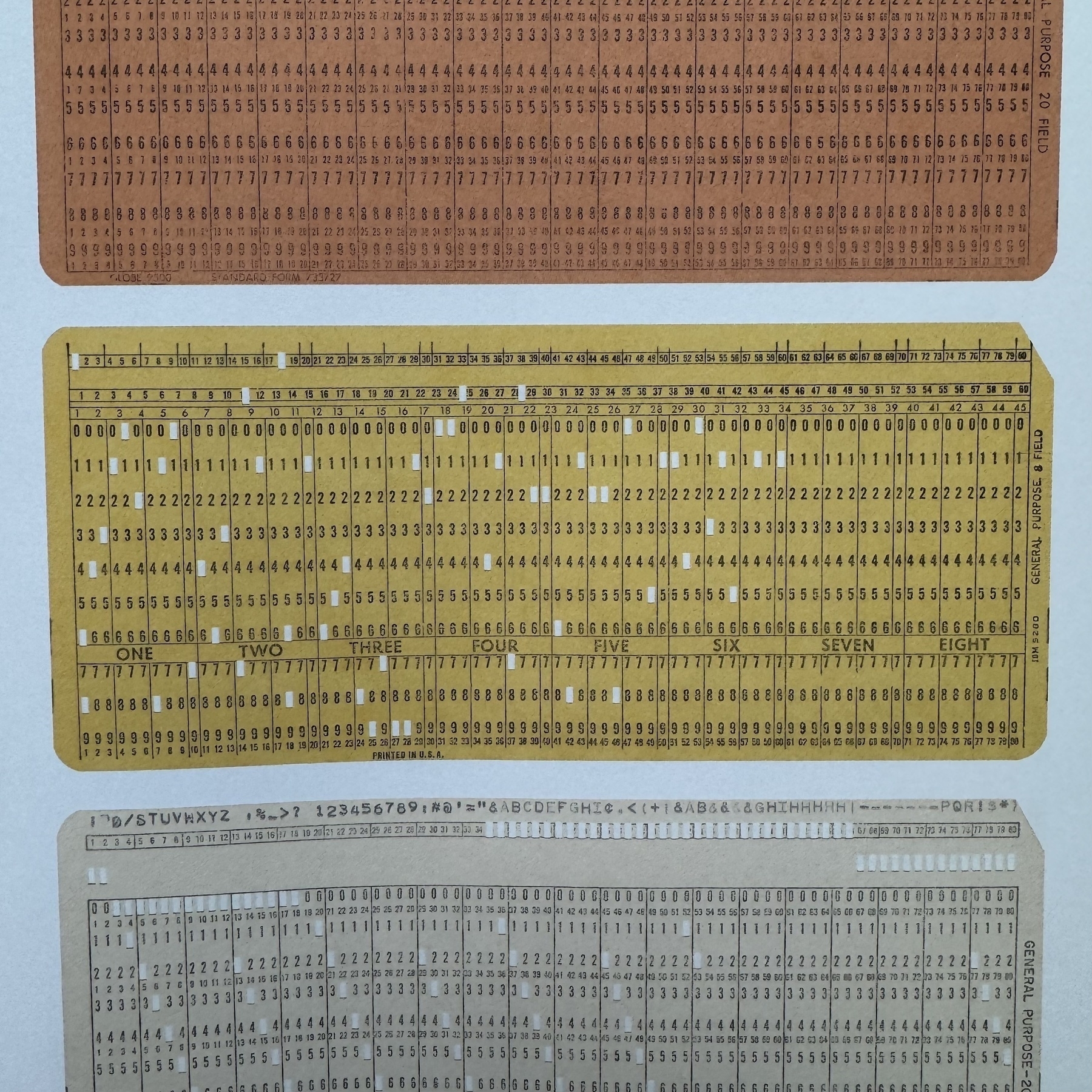 Vintage rectangular punch cards from the early computing era, featuring rows of tiny numbers with a smattering of punched holes to represent data.