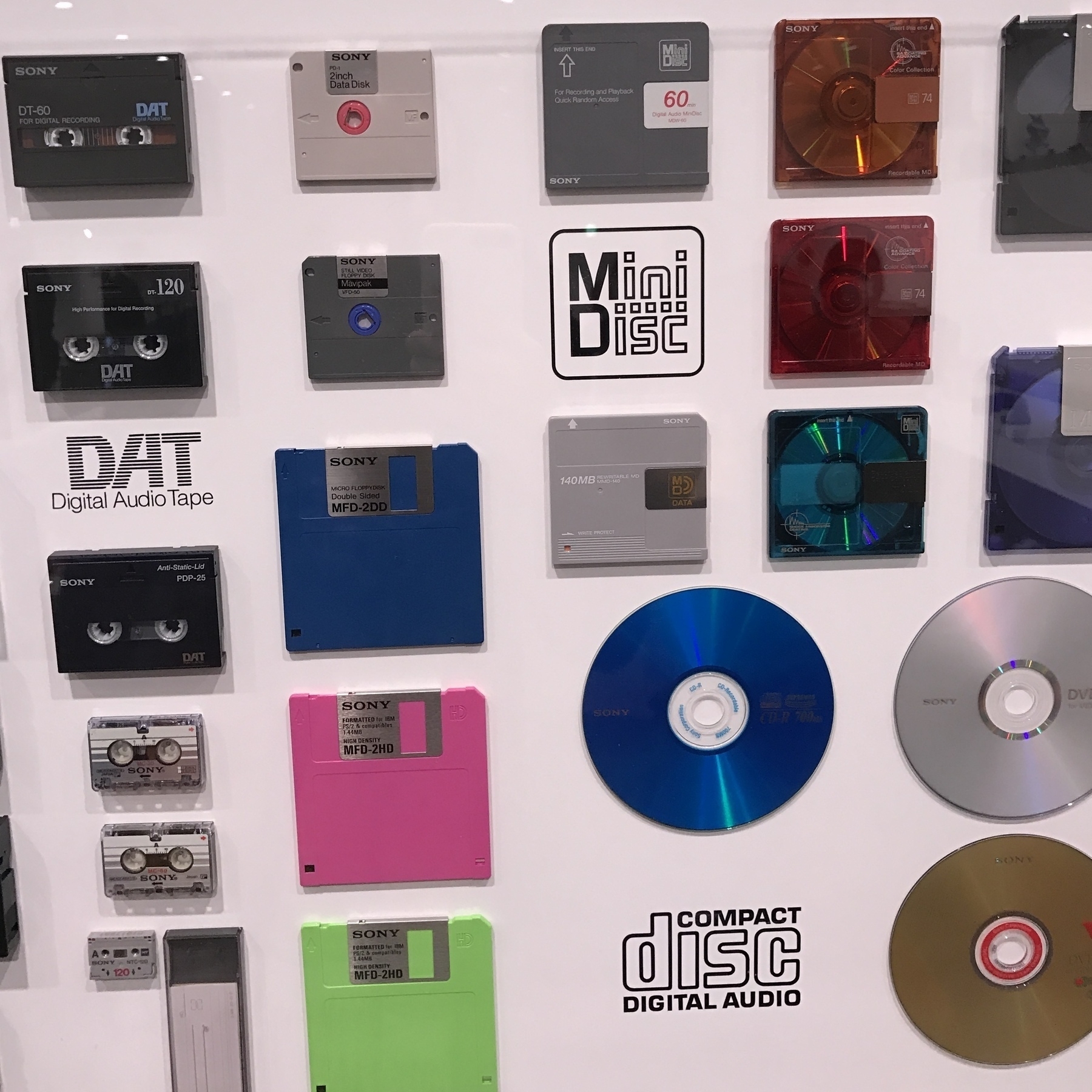 A wall exhibit of small physical media formats on display at SONY's headquarters in Tokyo, including micro-cassette, DAT, MiniDisc, and CD.