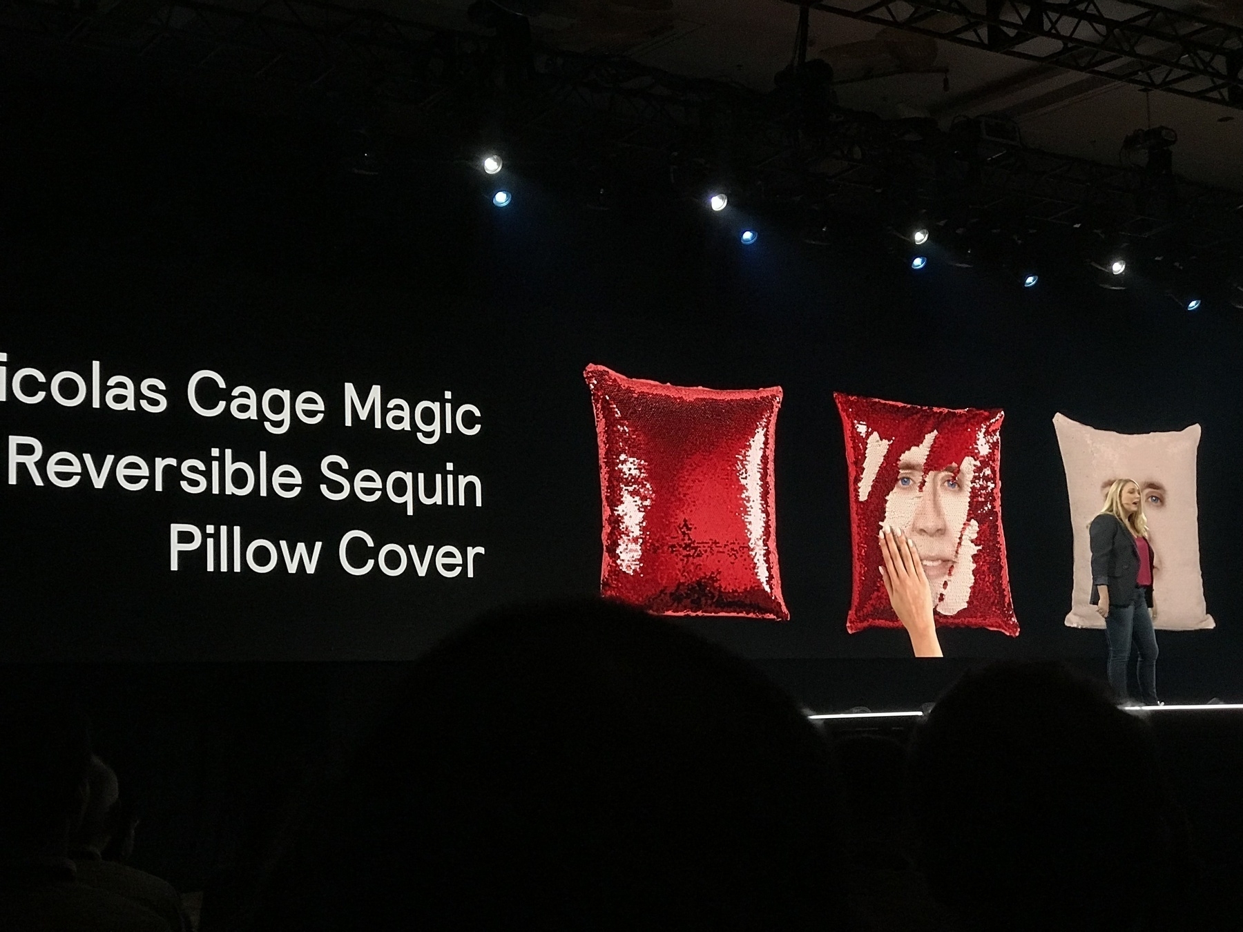 A keynote presenter on stage. The large slide behind them shows a red sequin pillow case with the face of Nicolas Cage hiding behind the sequins.