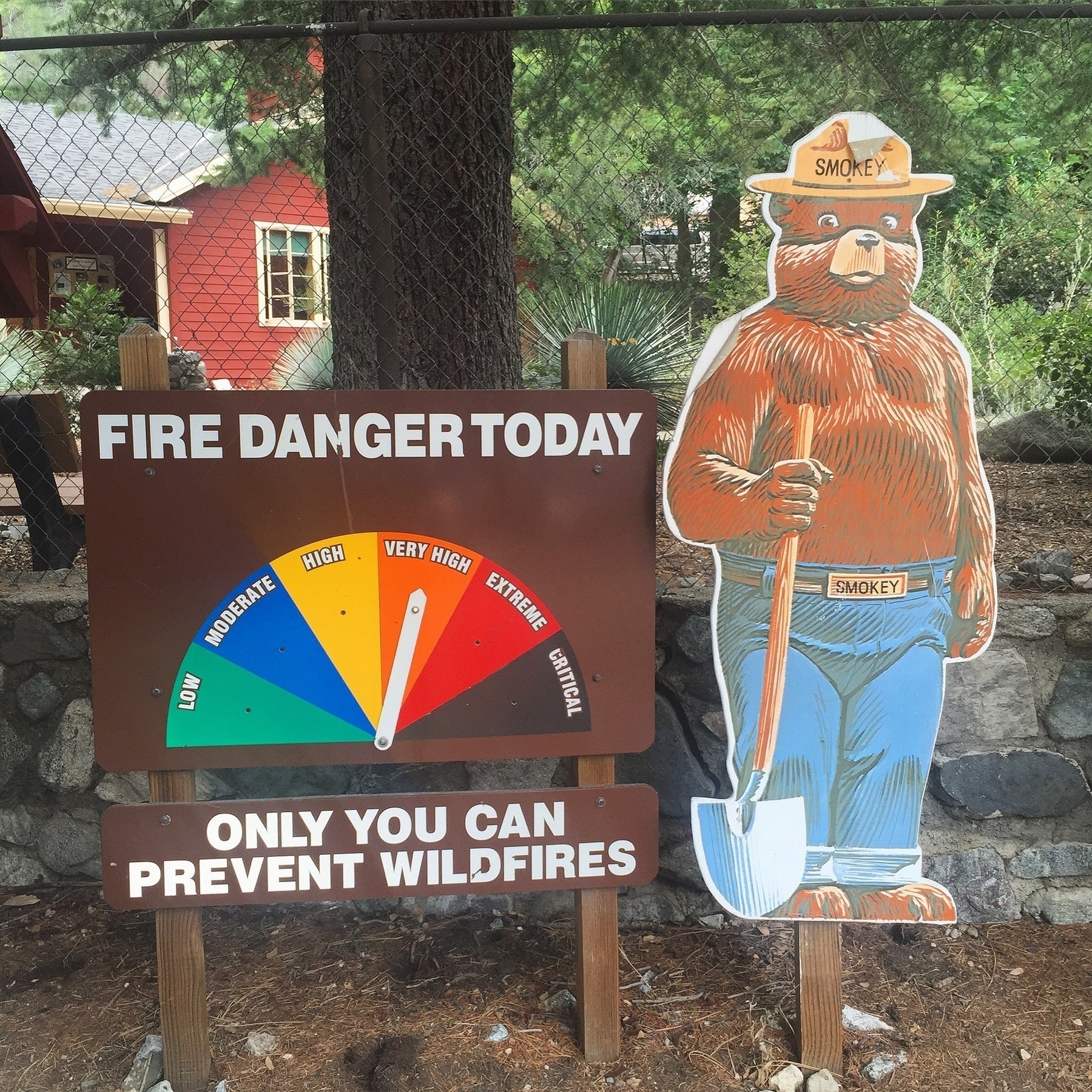 A Smokey The Bear cartoon sign in the woods, with a fire danger rating of 'Very High' and a reminder that 'Only You Can Prevent Wildfires'.